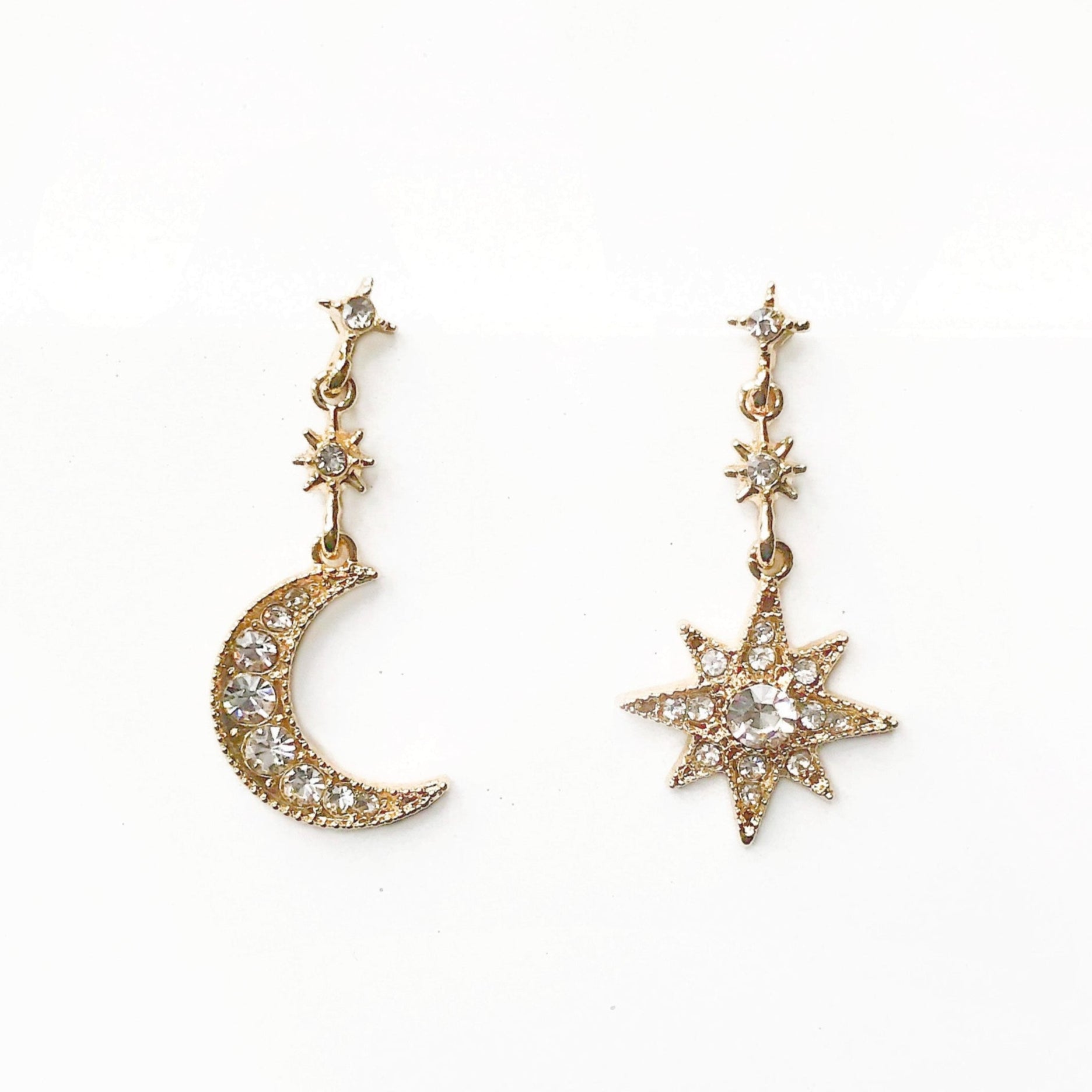 Gold earrings shaped like a moon and a star on a white background