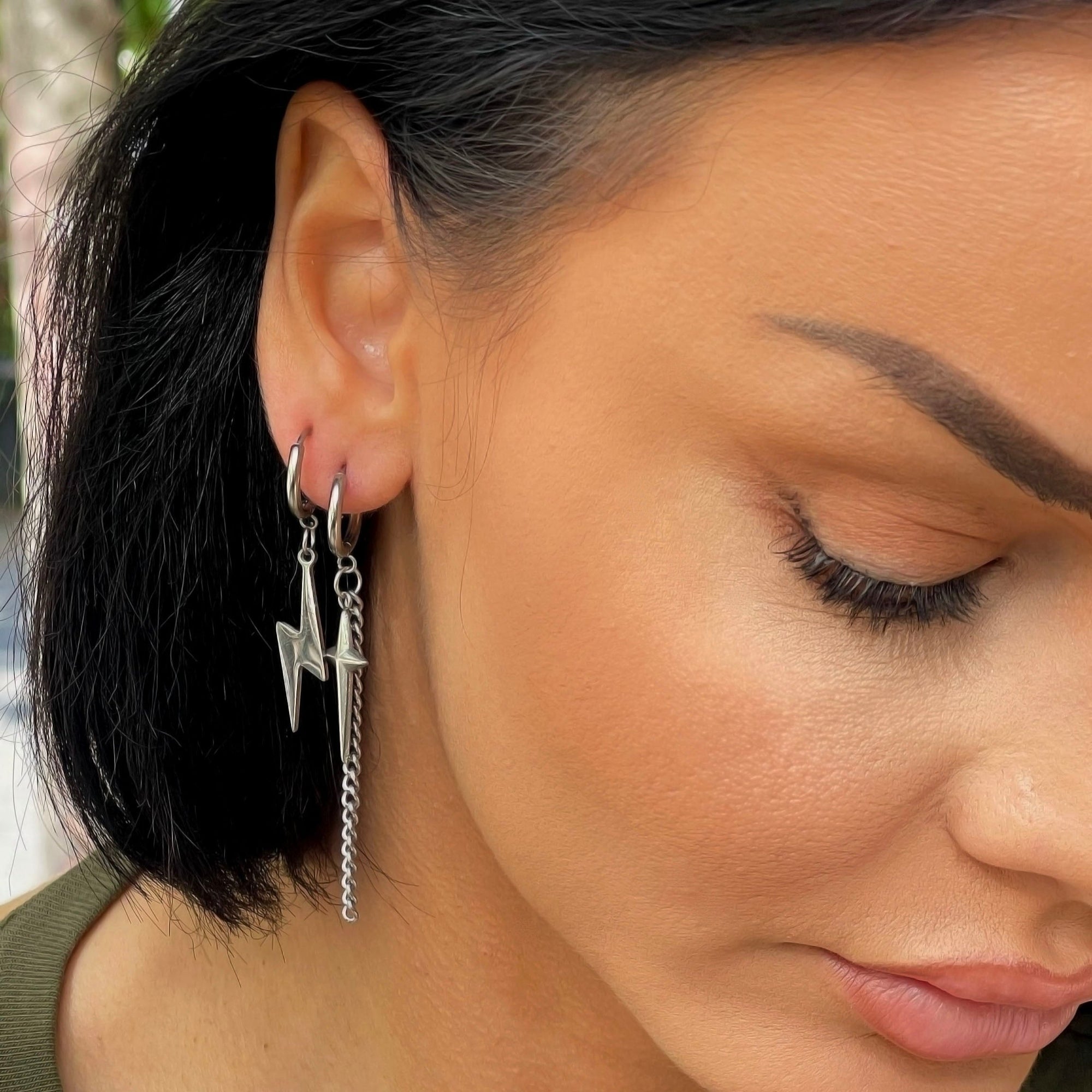 A close-up image of a woman's ear wearing a silver dangle earring with a cross and lightening bolt design.