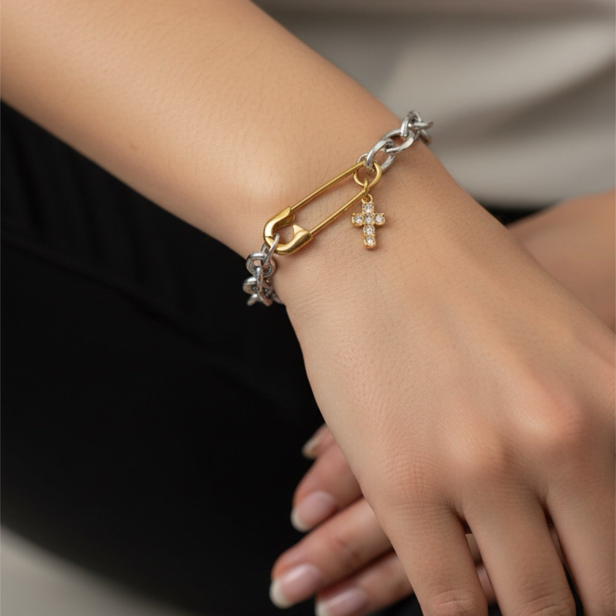 Bracelet with gold and silver charms on a wrist against a neutral background