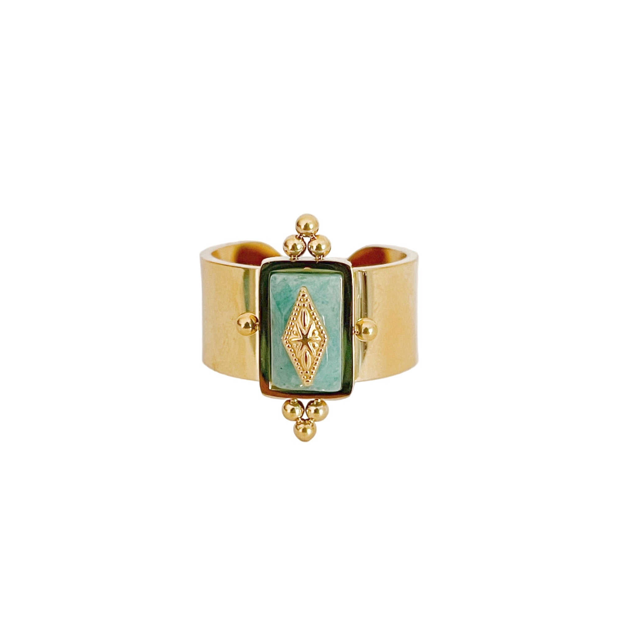 A gold-colored wide band ring featuring a rectangular turquoise crystal with intricate detailing on the sides.