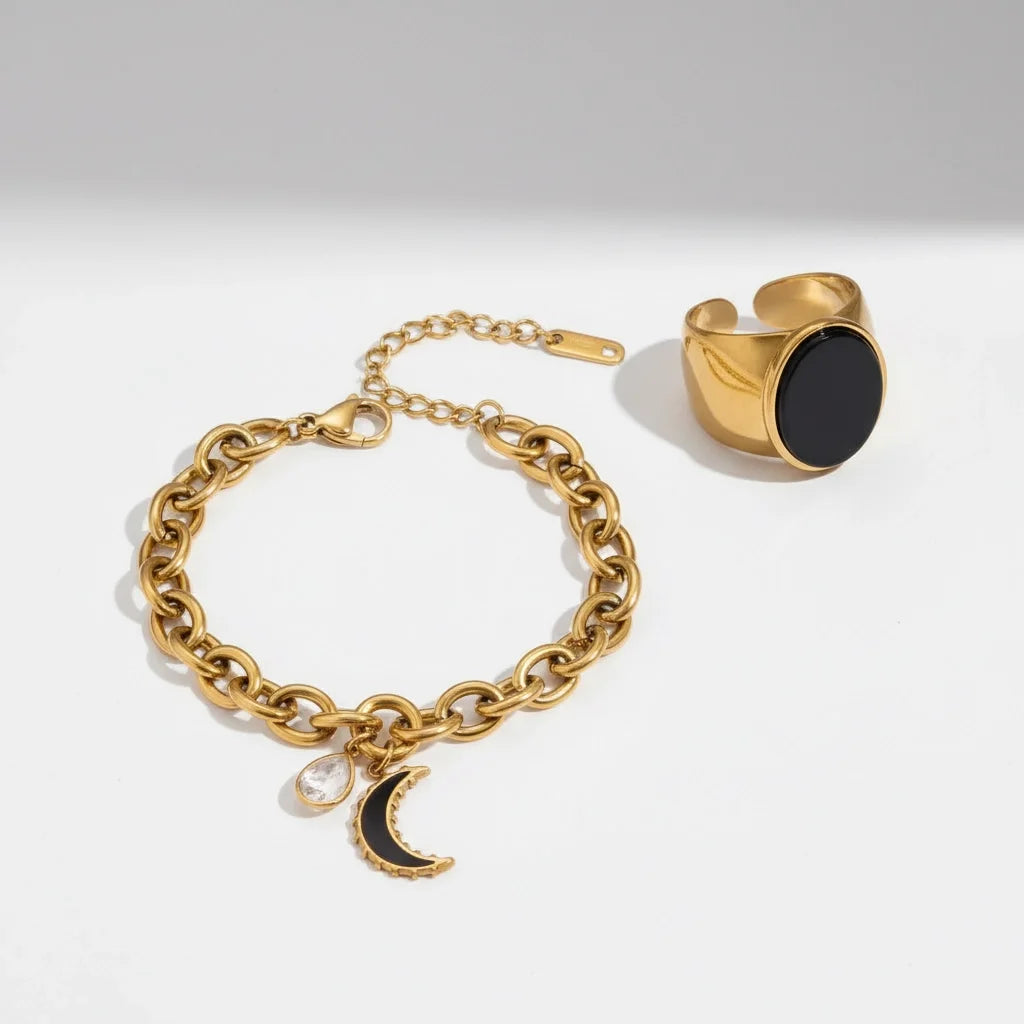 Gold bracelet with moon charm and gold ring with black stone on a white background
