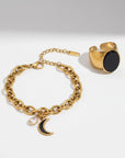 Gold bracelet with moon charm and gold ring with black stone on a white background